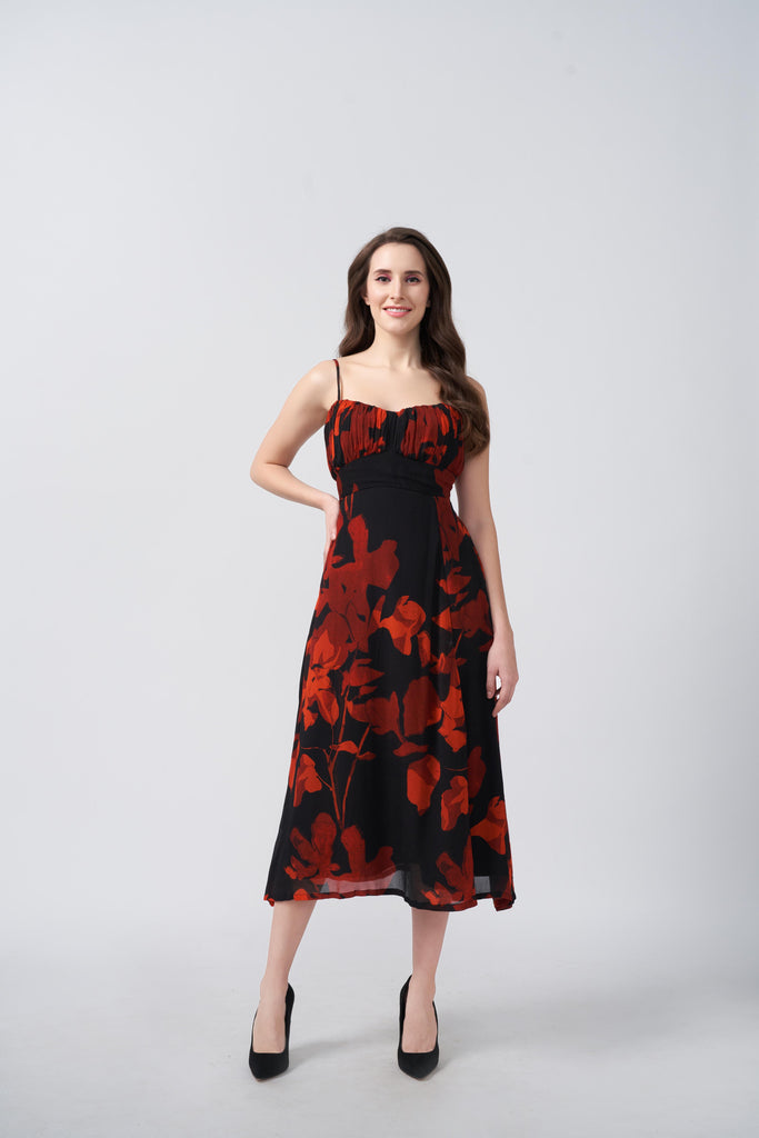Front view of model wearing an orange and black abstract floral midi dress with spaghetti straps