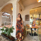 Woman wearing chinon maxi dress with bow detail and multi-color abstract print in earthy and vibrant tones, House of Varada.