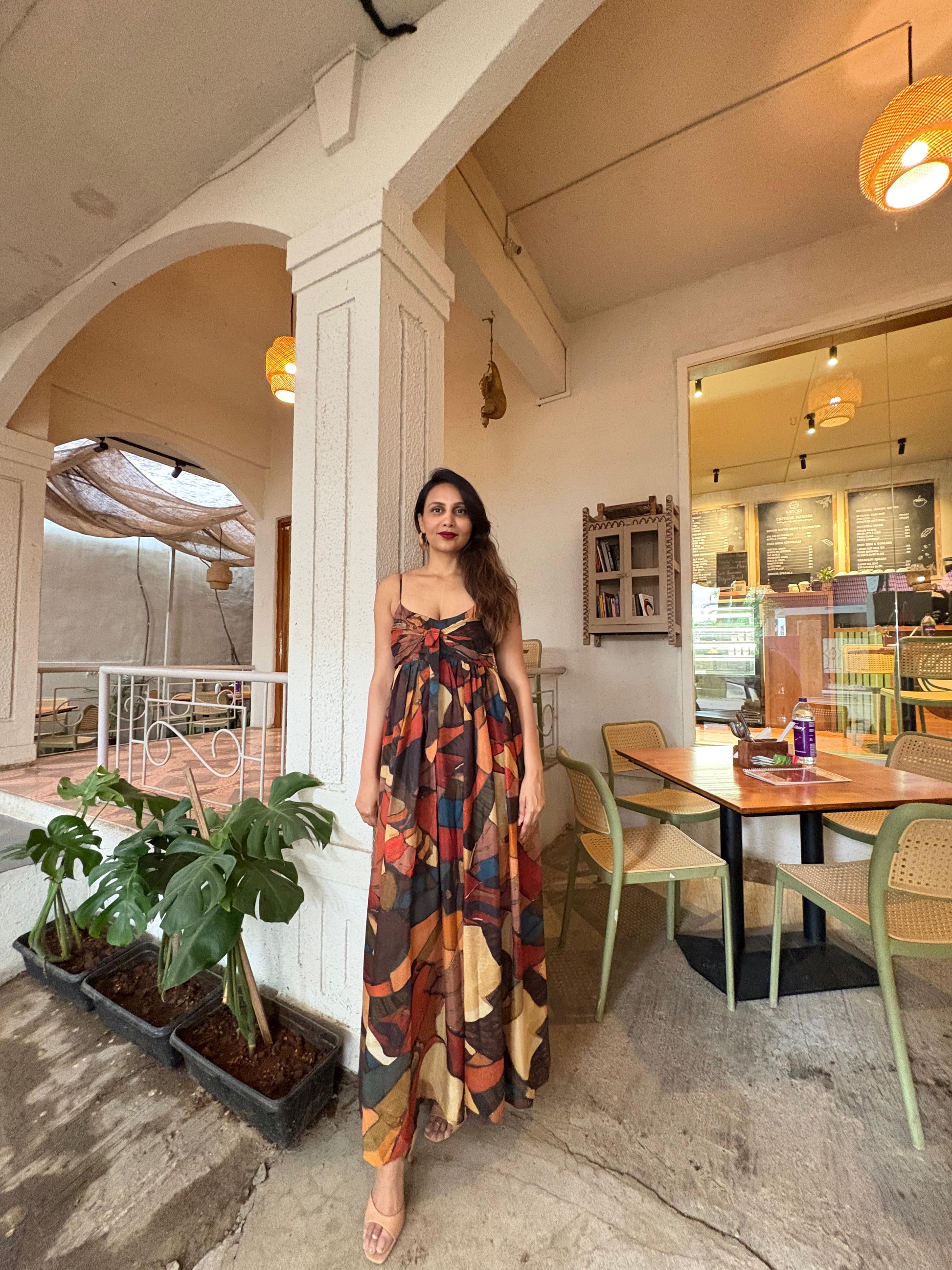 Woman wearing chinon maxi dress with bow detail and multi-color abstract print in earthy and vibrant tones, House of Varada.