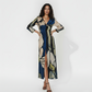 Full-length maxi dress featuring a high front slit and a sophisticated twist detail at the bodice. The design showcases an oversized abstract print in a palette of deep navy, sage green, and cream, making it a statement piece for semi-formal evening events.