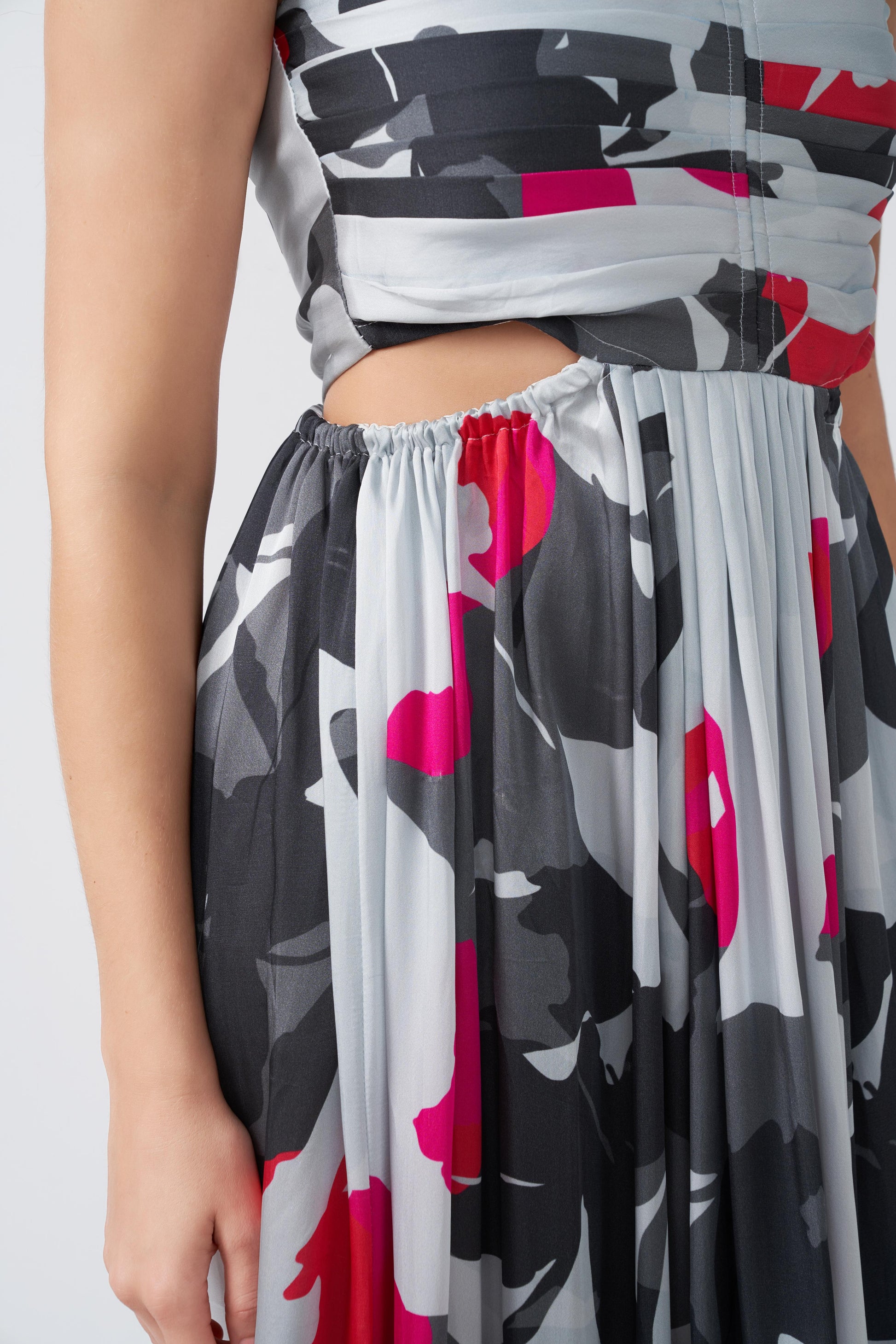 Close-up of waist cut and pleated skirt detailing on pink, grey, and charcoal abstract midi dress.