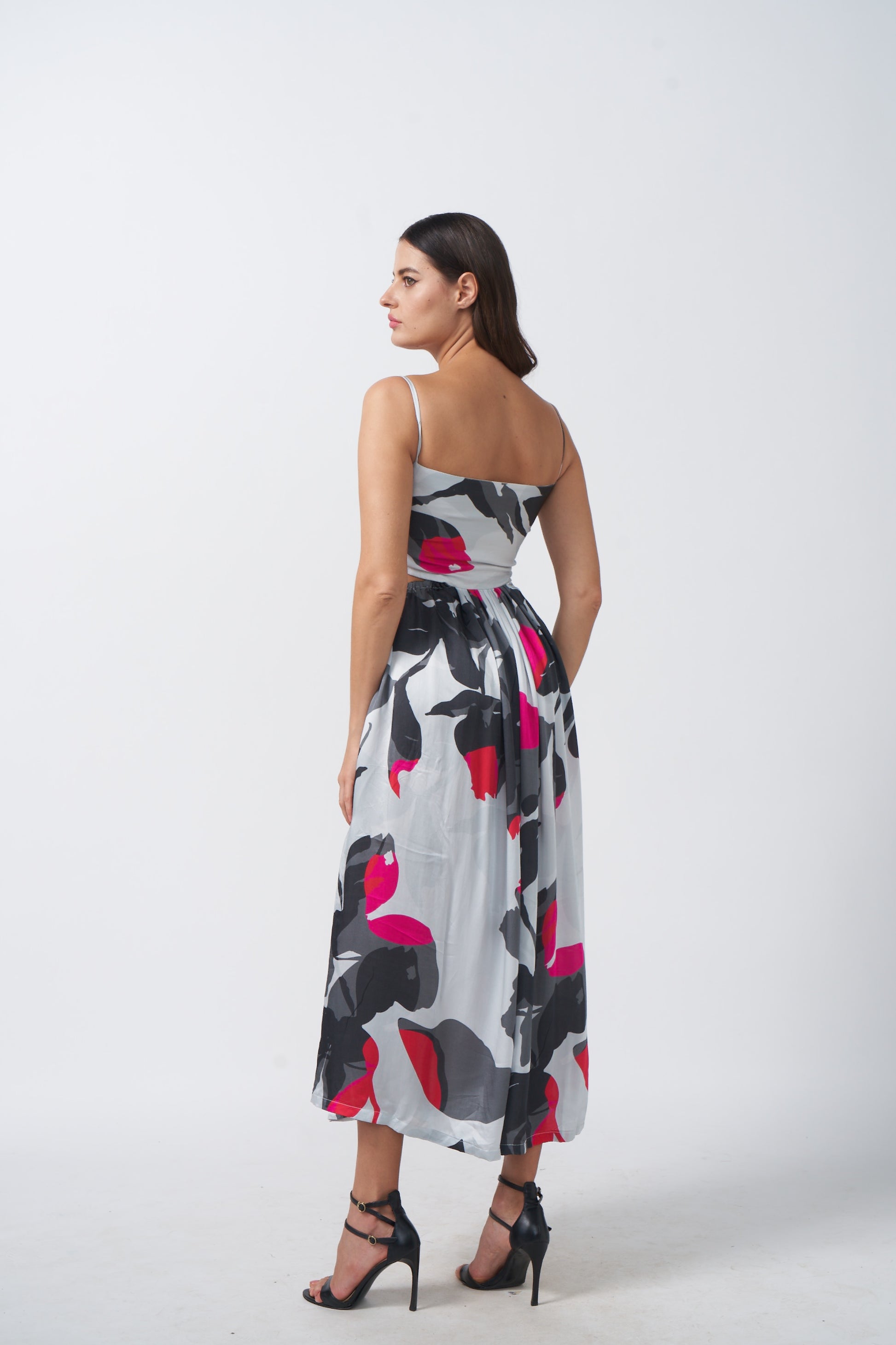 Side-back studio view of model wearing abstract print midi dress with defined waist cuts and flow.