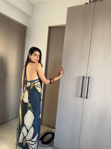 Model standing by wardrobe in navy and beige floral halter dress, offering a casual indoor styling view.