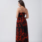 Back view of a woman in a red and black floral chiffon dress with spaghetti straps, standing outdoors