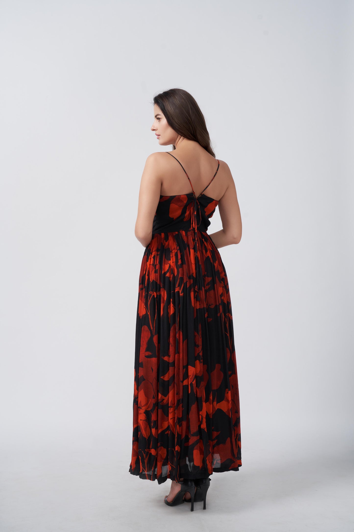 Back view of a woman in a red and black floral chiffon dress with spaghetti straps, standing outdoors