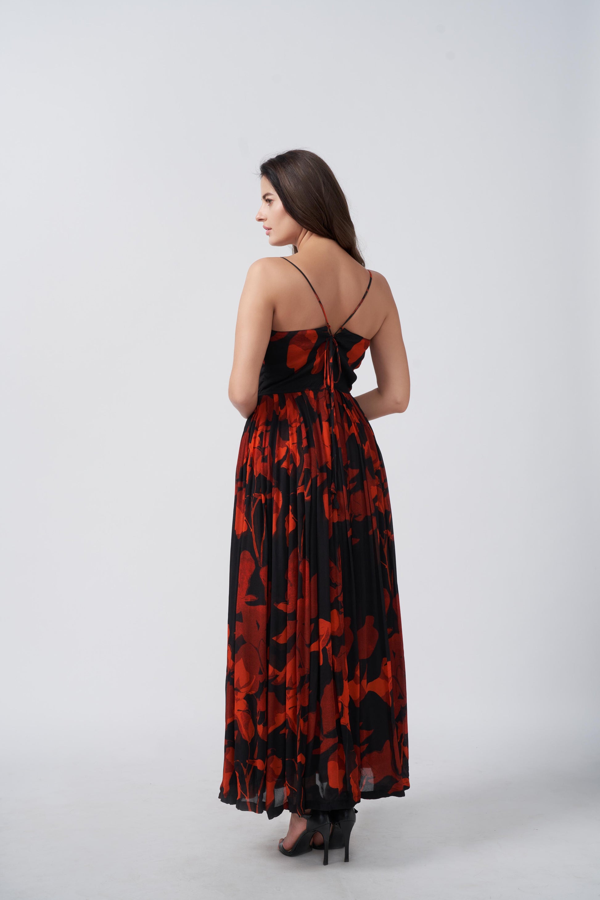 Back view of a woman in a red and black floral chiffon dress with spaghetti straps, standing outdoors
