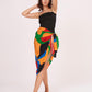 Model mid-walk with one arm raised, showing the side draping of the colorful sarong wrap paired with the fitted black dress.
