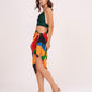 Side profile view showcasing the breezy, leg-baring cut of the Beach Sarong Wrap paired with a green halter top. The colorful geometric print creates a vibrant look for summer vacations.