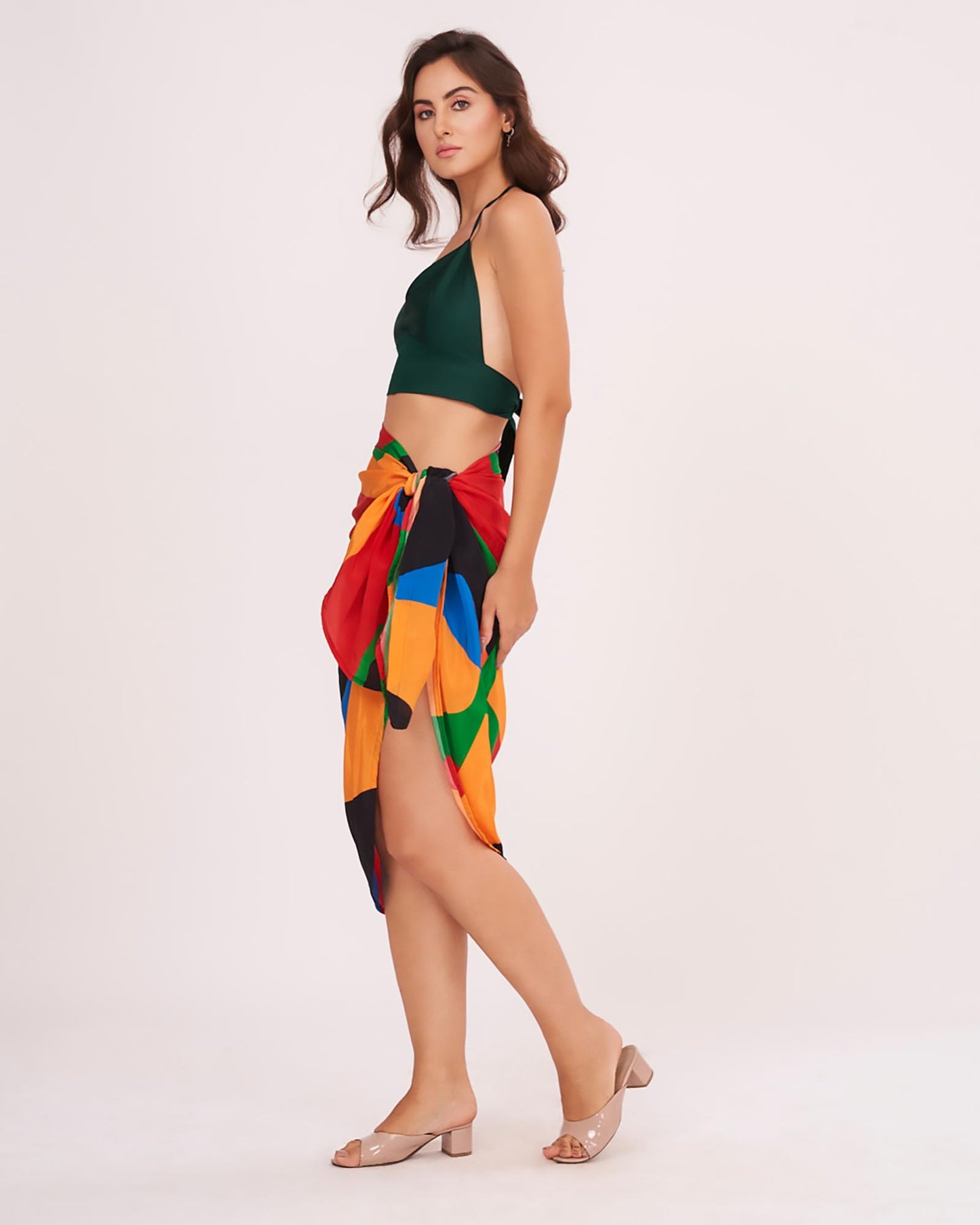Side profile view showcasing the breezy, leg-baring cut of the Beach Sarong Wrap paired with a green halter top. The colorful geometric print creates a vibrant look for summer vacations.