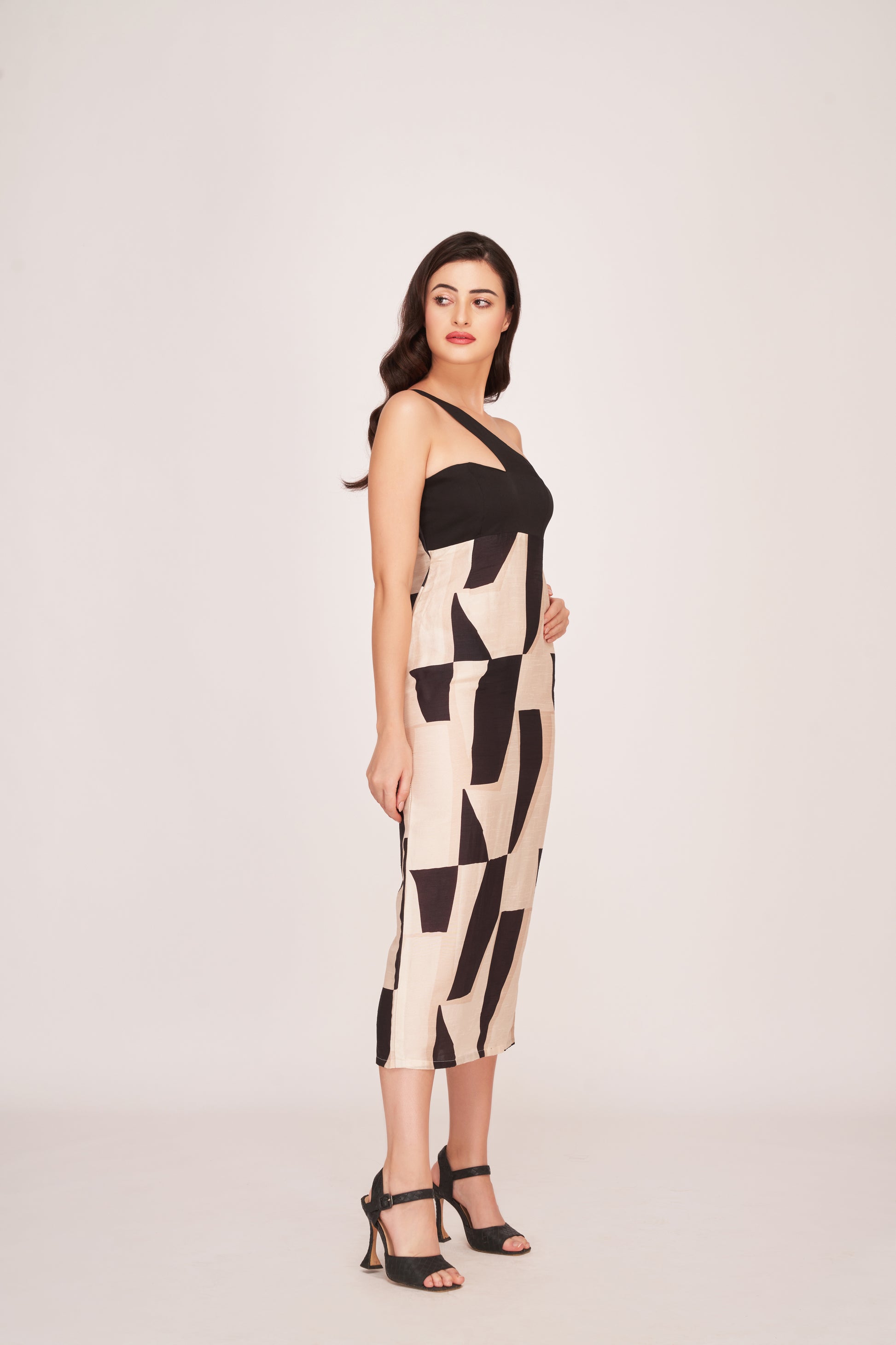 Model posing with one hand on her waist in the black abstract midi dress, highlighting the asymmetric neckline.