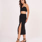 Side walking pose highlighting the one-sleeve silhouette and the clean slit cut of the skirt.