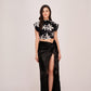 Model wearing a black floral printed co-ord set with a broad-shoulder crop top and high-slit skirt.