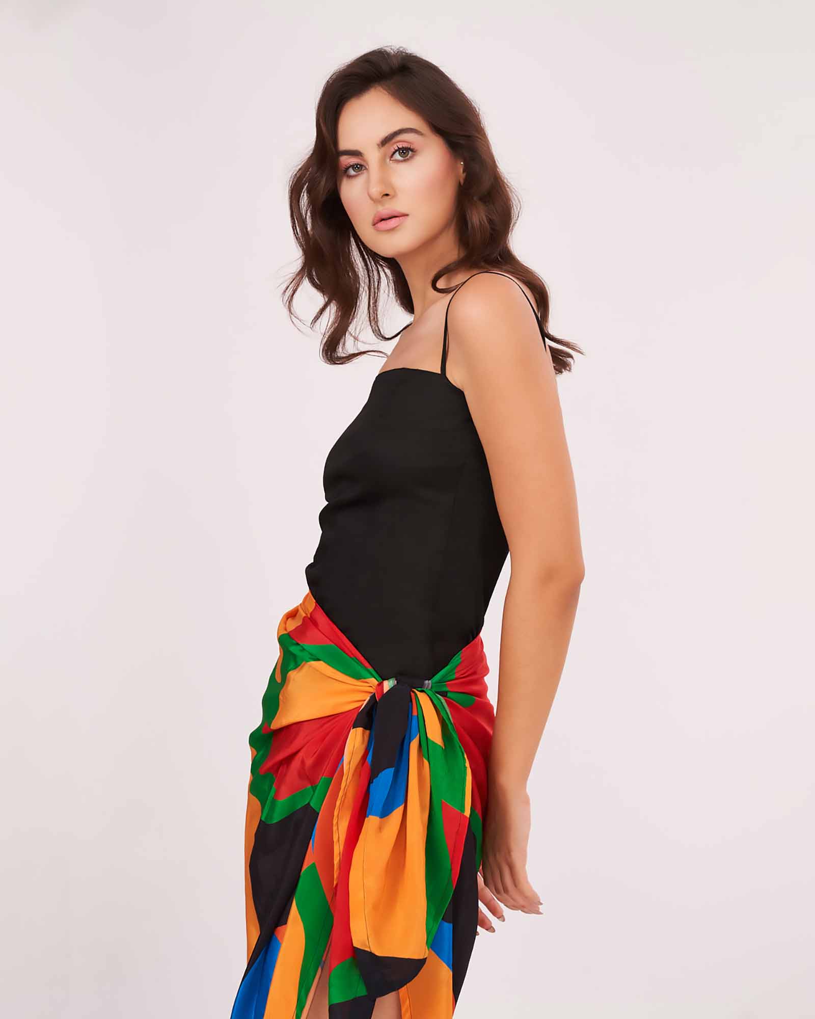 Model in close-up front-facing pose showcasing the square-neck black mini dress and vibrant sarong tied at the waist.