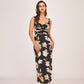 Model posing in a black satin ankle-length dress with beige floral print and twisted neckline, highlighting the elegant front view.