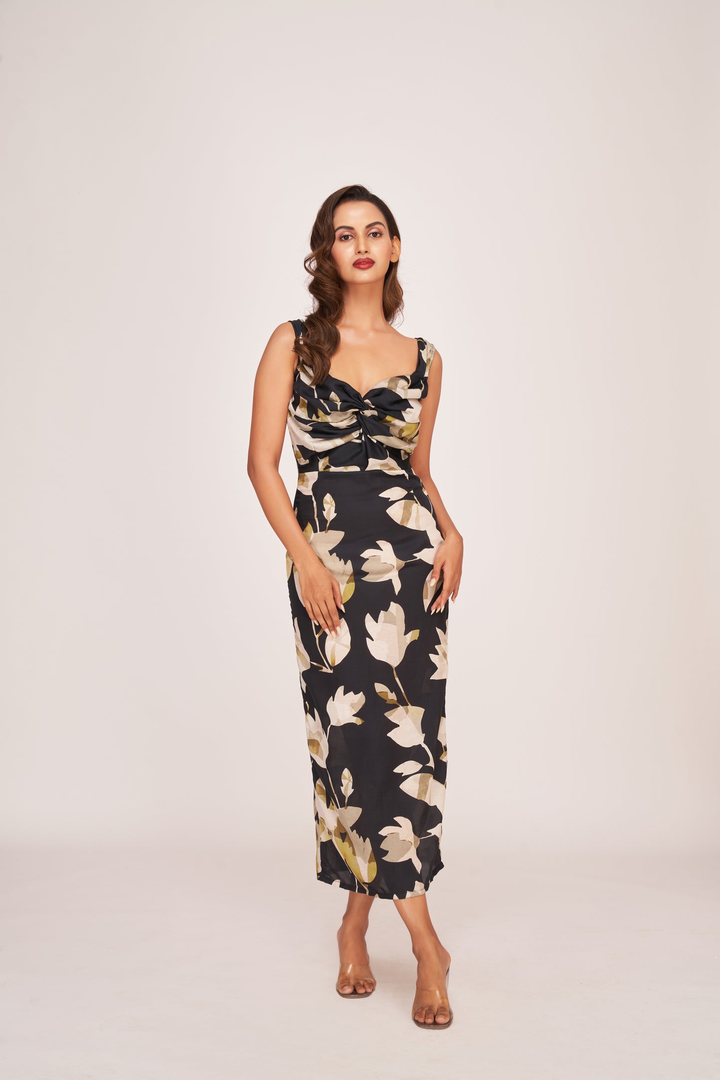 Model posing in a black satin ankle-length dress with beige floral print and twisted neckline, highlighting the elegant front view.