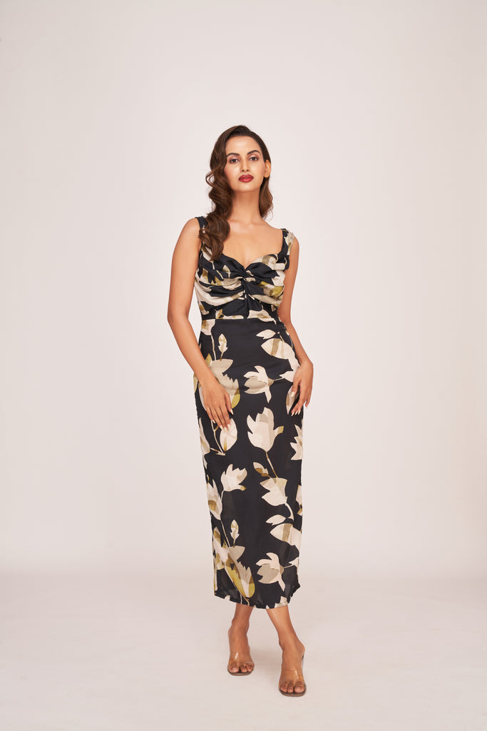 Model posing in a black satin ankle-length dress with beige floral print and twisted neckline, highlighting the elegant front view.