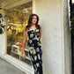 Outdoor shot of the model walking in a black floral print midi dress with strap shoulders, capturing natural movement and poise.