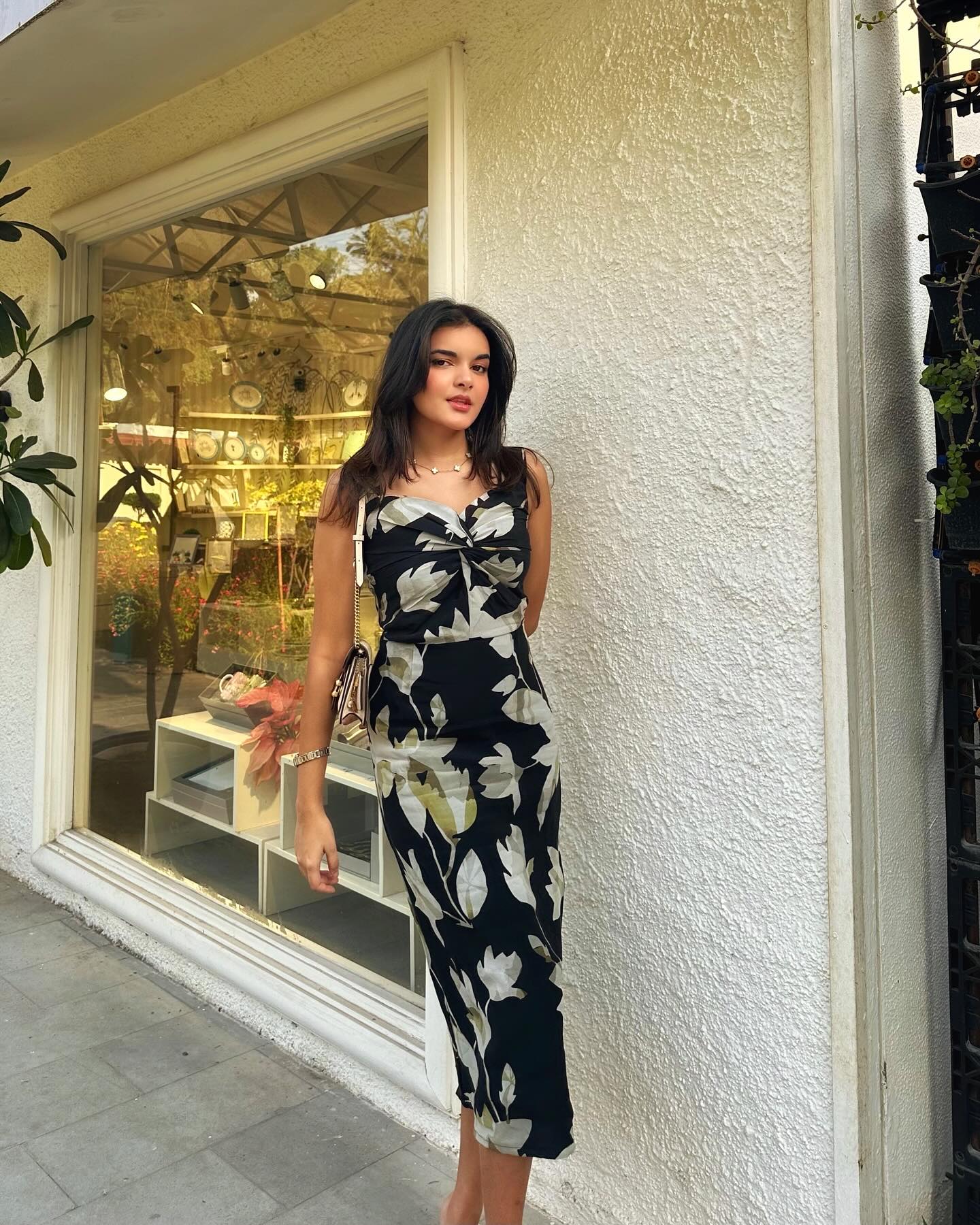 Outdoor shot of the model walking in a black floral print midi dress with strap shoulders, capturing natural movement and poise.
