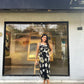 Model standing in front of a store wearing the black satin floral midi dress, emphasizing the urban styling versatility.