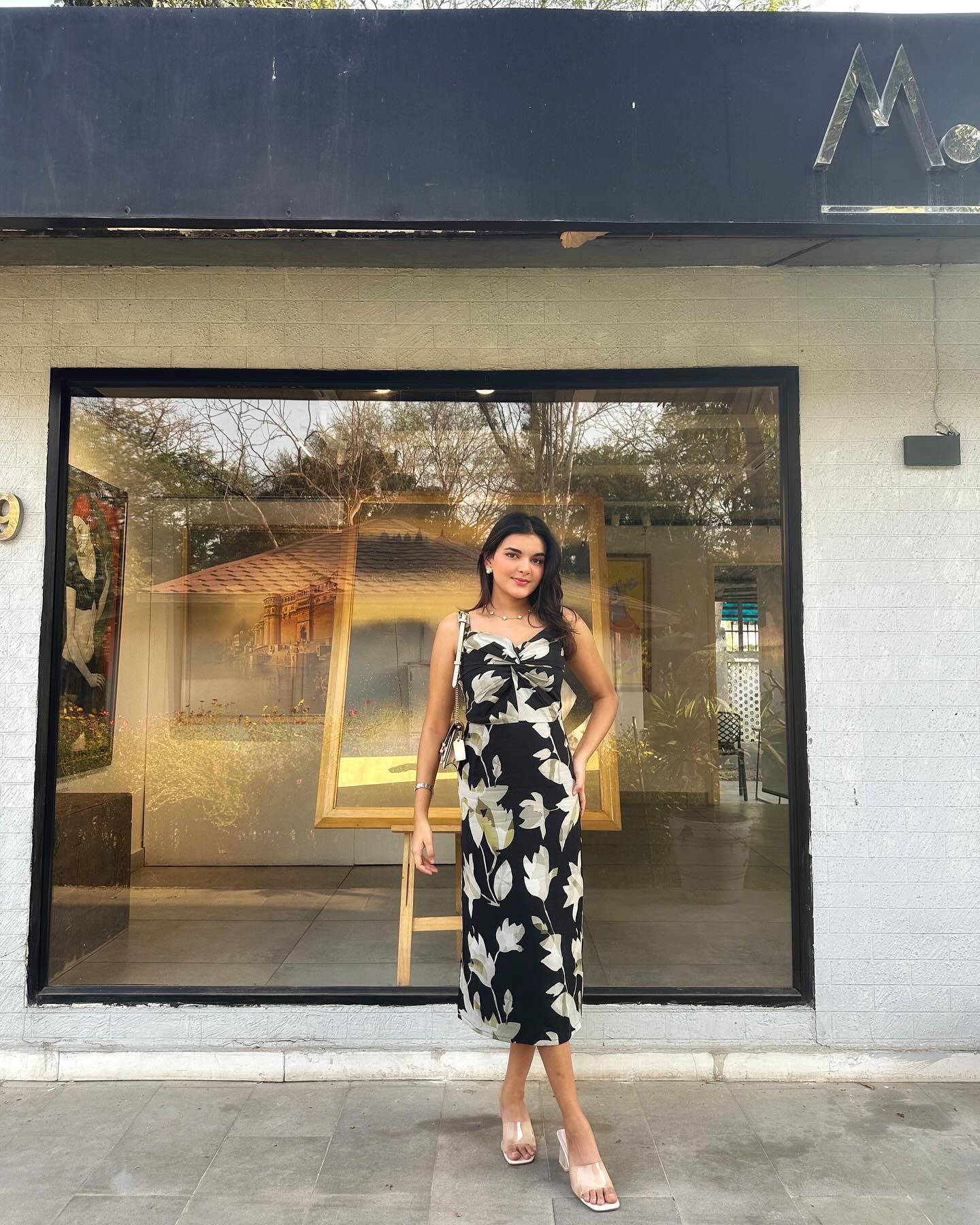 Model standing in front of a store wearing the black satin floral midi dress, emphasizing the urban styling versatility.