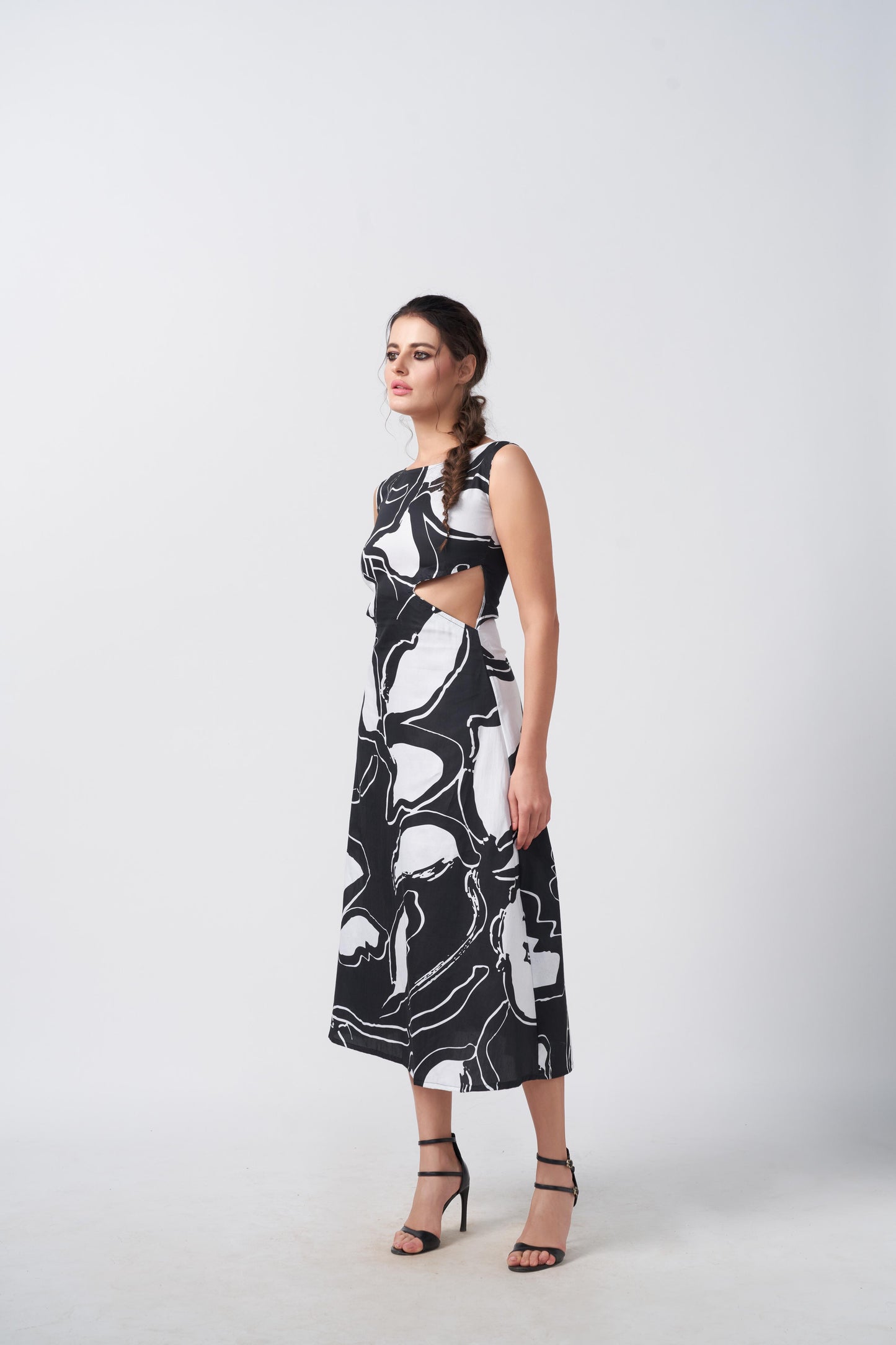 Side view of the model walking in sleeveless black and white abstract dress, highlighting the waist cut-out detail.