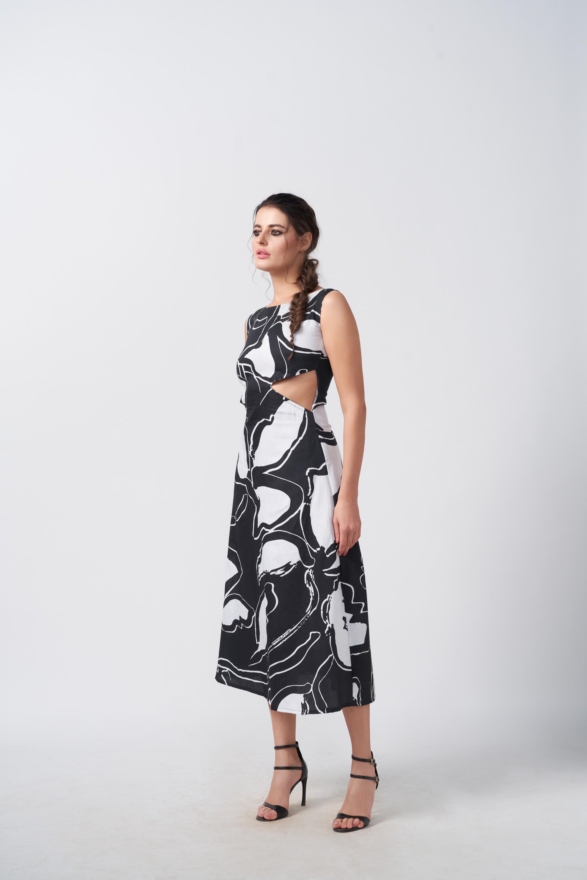 Side view of the model walking in sleeveless black and white abstract dress, highlighting the waist cut-out detail.
