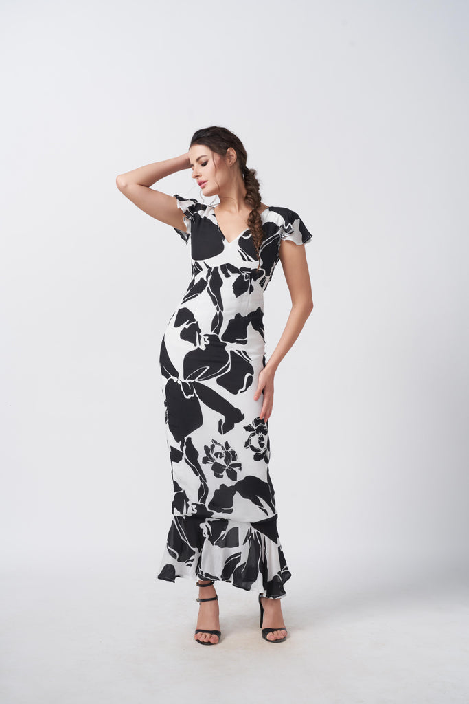 Model standing with hand on head in black and white floral crepe dress with V-neck and ruffle sleeves.