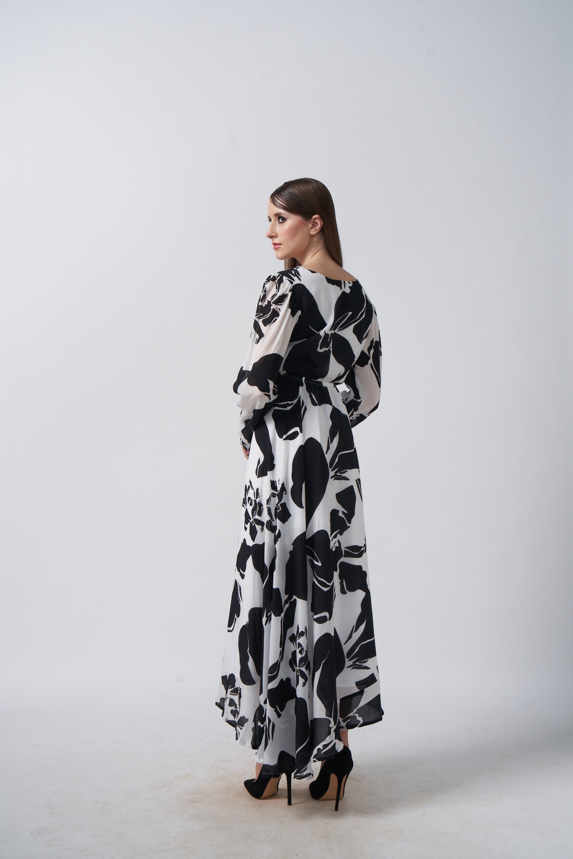 Model in side pose highlighting the side slit and sleeve drape of the black and white floral dress.