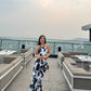 Model standing on a rooftop in black and white abstract halter dress, facing camera with city view behind.