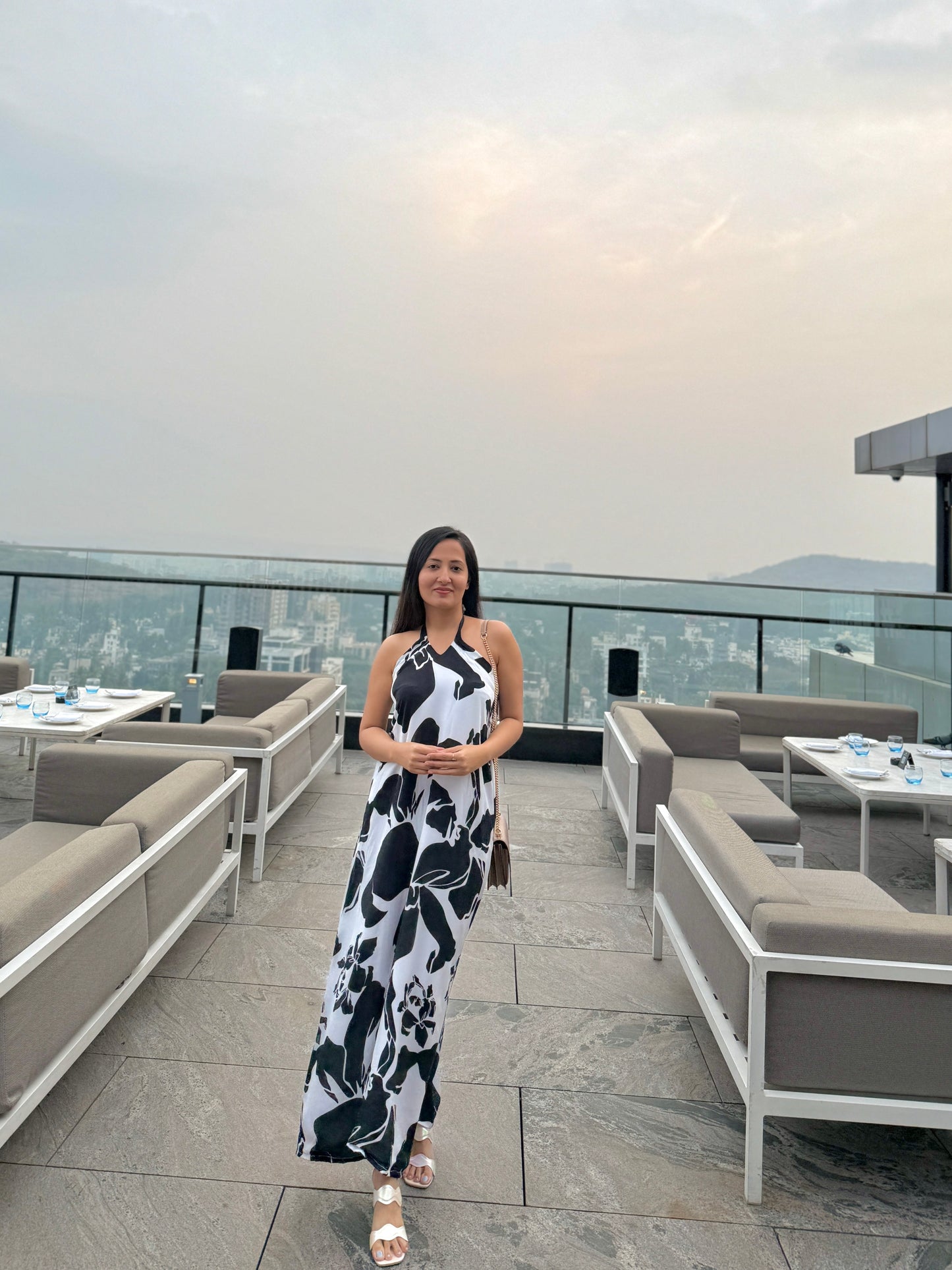 Model standing on a rooftop in black and white abstract halter dress, facing camera with city view behind.