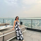 Model seated on rooftop in black and white dress, capturing relaxed elegance and scenic backdrop.