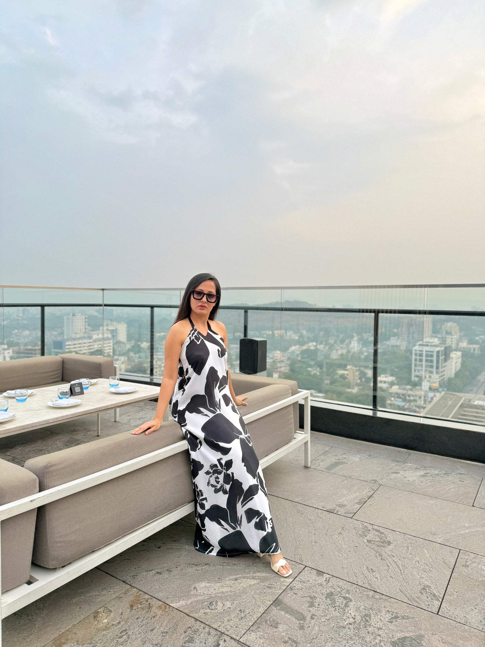 Model seated on rooftop in black and white dress, capturing relaxed elegance and scenic backdrop.