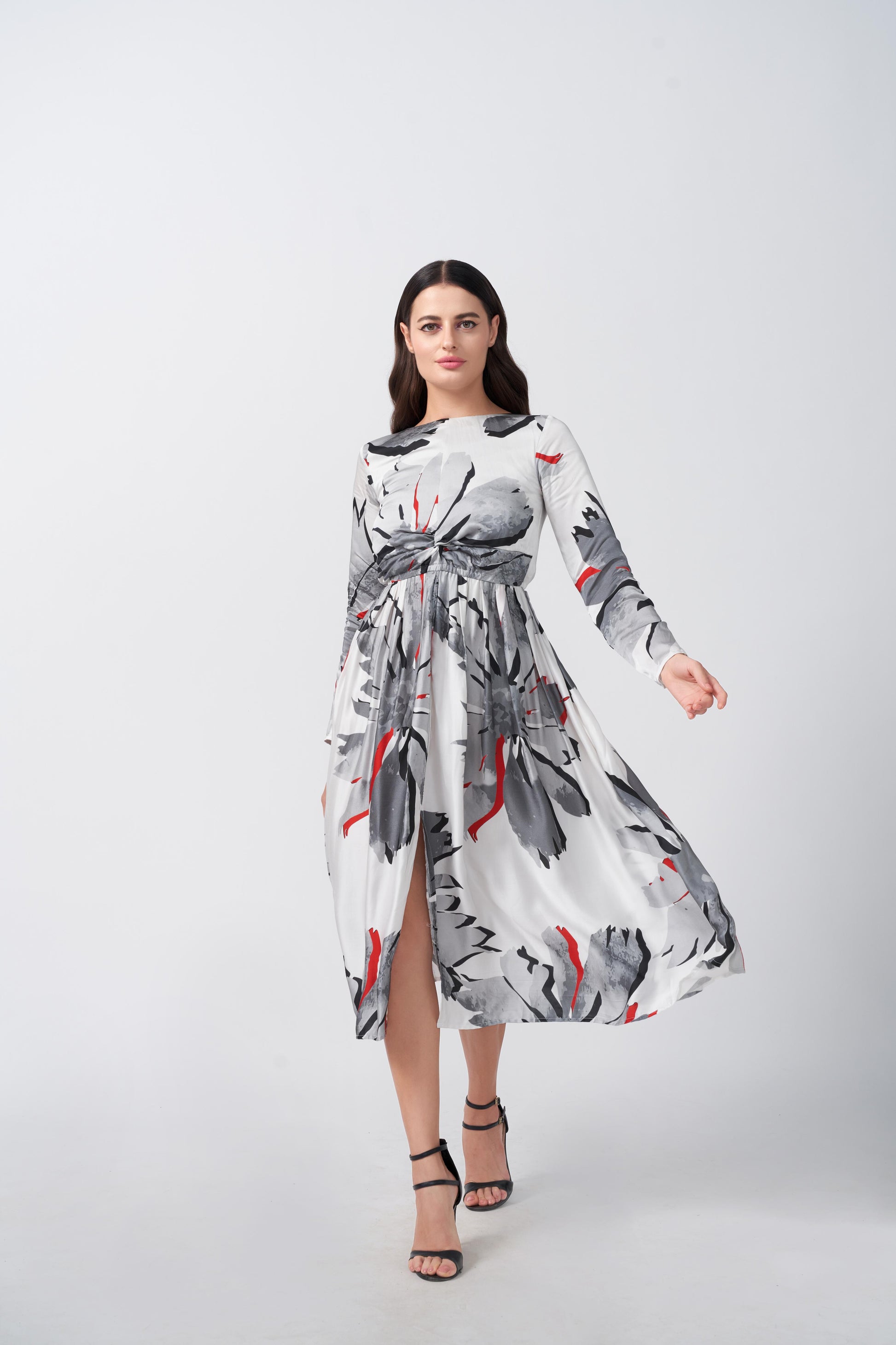 Model walking in a white and grey satin floral dress with red accents and knot front detail.