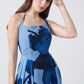 Model in light and dark blue floral halter dress, hand on head, showcasing a soft, elegant expression.