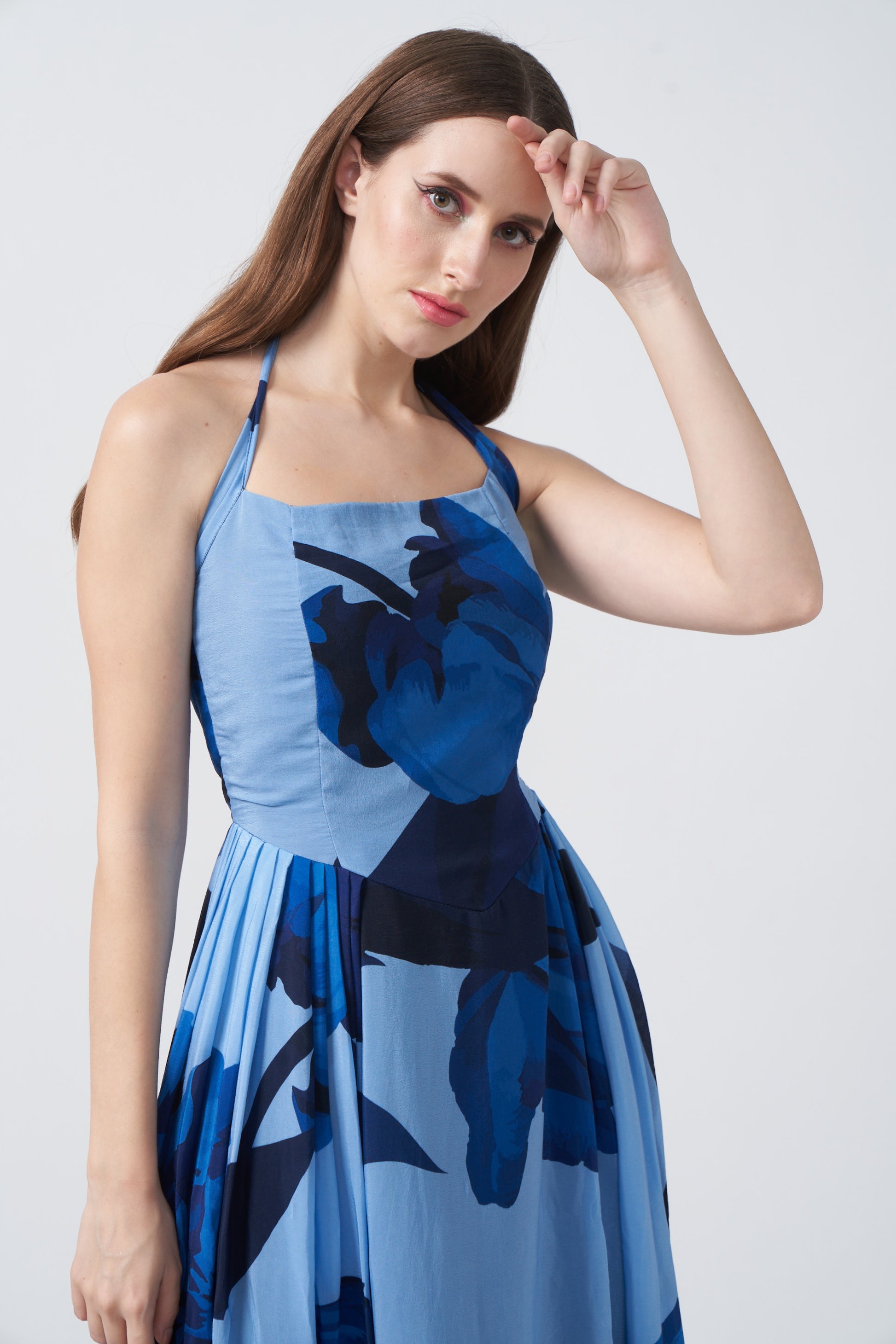 Model in light and dark blue floral halter dress, hand on head, showcasing a soft, elegant expression.