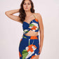Side-turned pose with one hand raised to head, showing the ruched halter neckline and flowy slit of the floral skirt in the blue co-ord set.