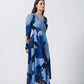 Walking view of model in blue floral crepe dress, showcasing ankle-length flow and slit detail.