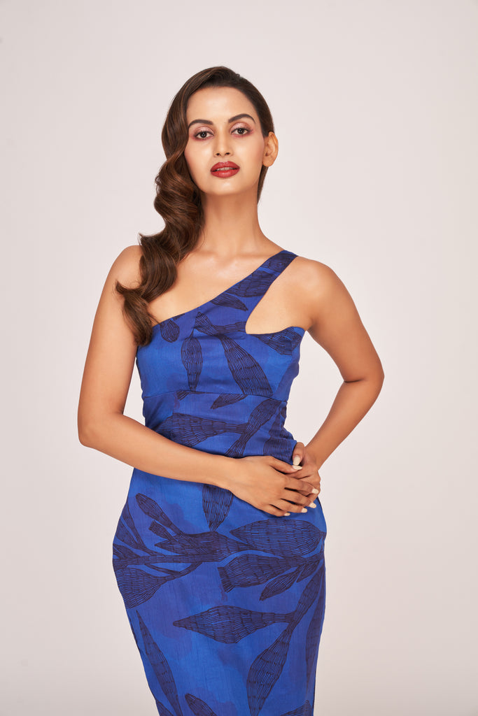 Model in a blue one-shoulder silk midi dress with floral digital print, standing front-facing with hands resting on waist.