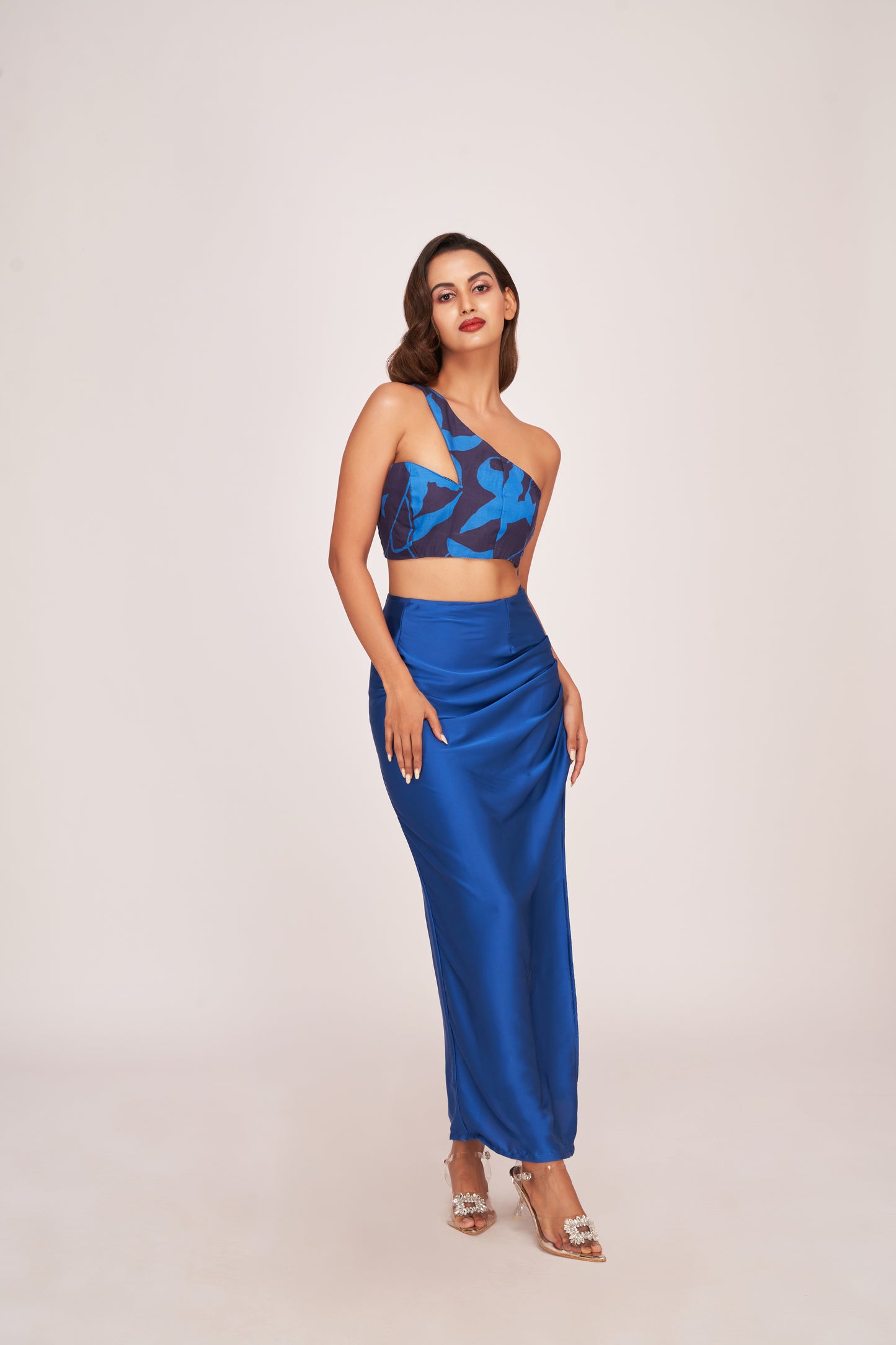 Full frontal pose of model in printed one-shoulder blue co-ord set with a side slit skirt and pleated detail.