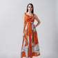 Model in burnt orange and white abstract cotton satin midi dress with twisted neckline, posing front-facing.