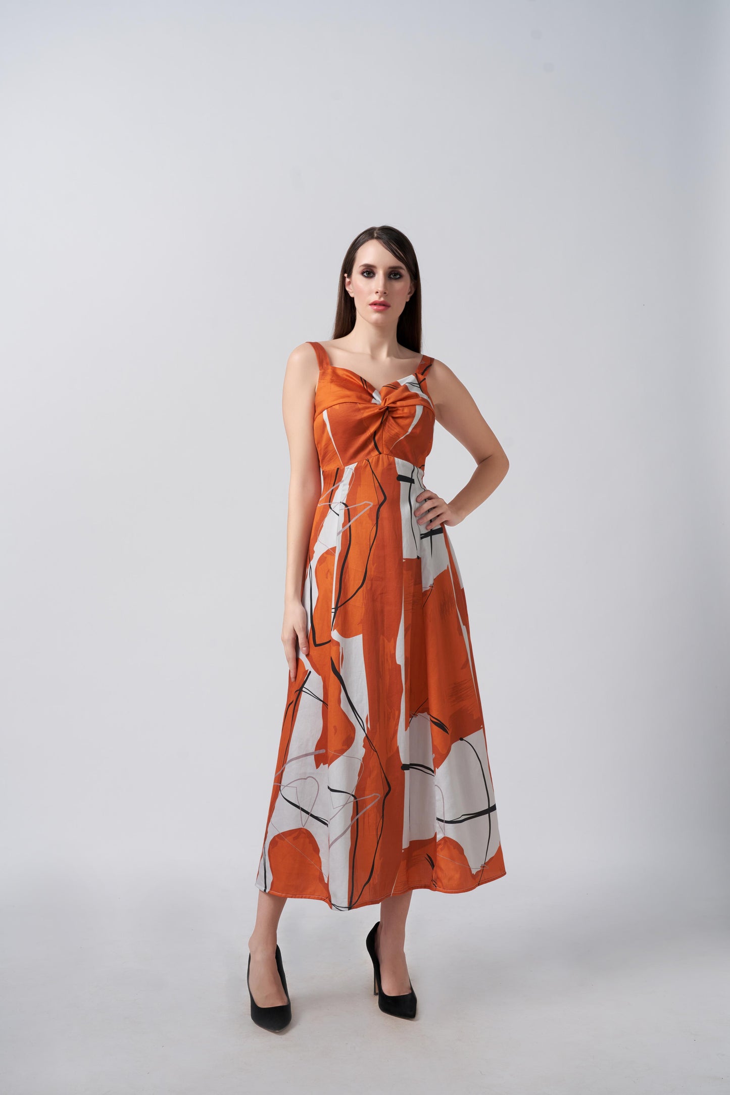 Model in burnt orange and white abstract cotton satin midi dress with twisted neckline, posing front-facing.