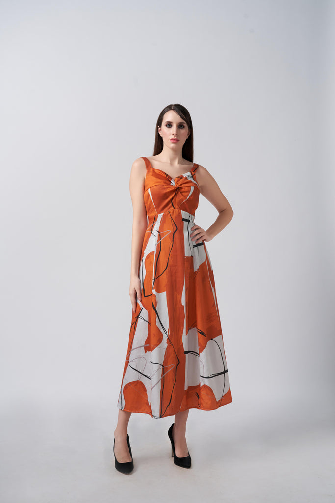 Model in burnt orange and white abstract cotton satin midi dress with twisted neckline, posing front-facing.