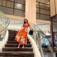 Model in burnt orange abstract print midi dress descending staircase, showcasing flow and outdoor styling.