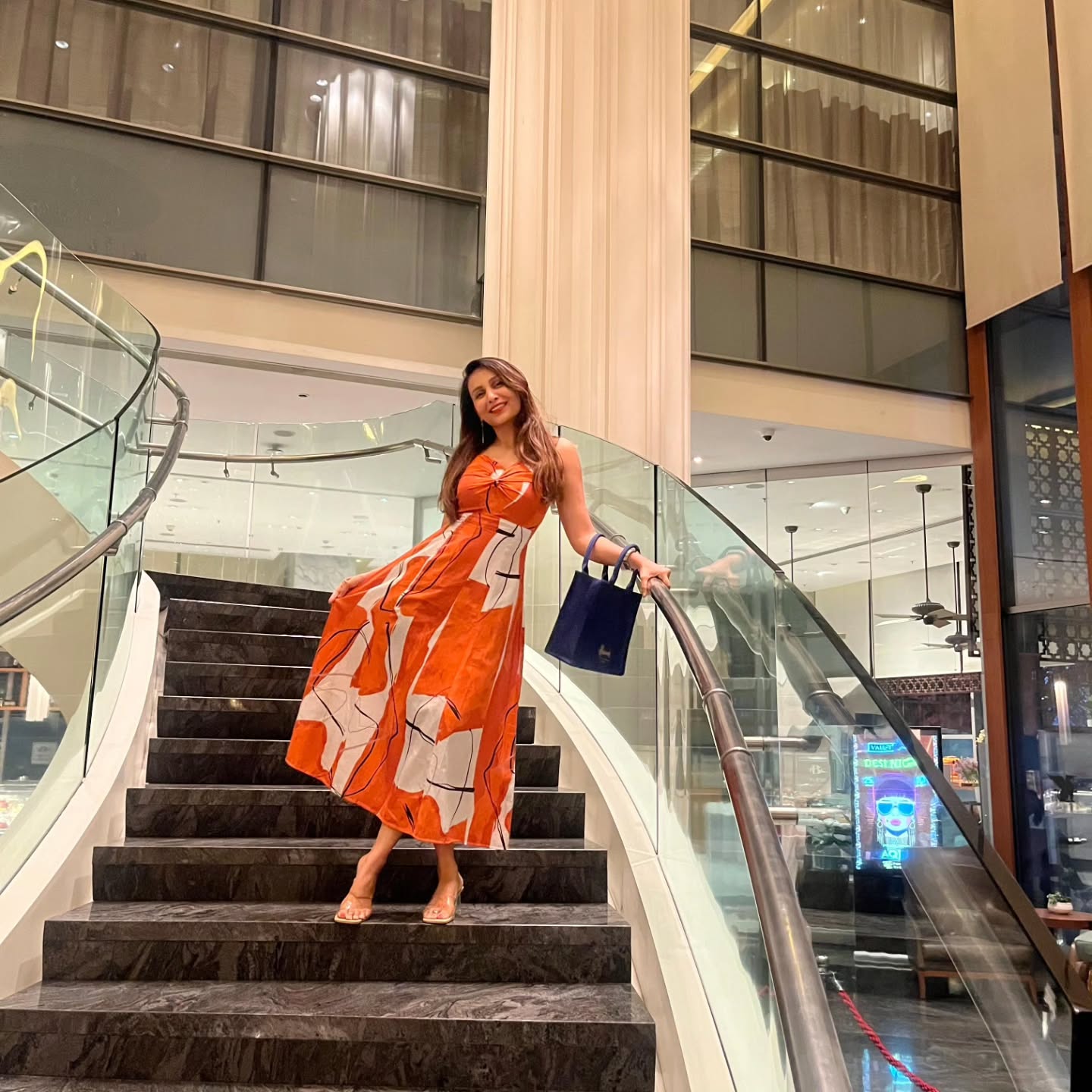 Model in burnt orange abstract print midi dress descending staircase, showcasing flow and outdoor styling.