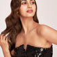 lose-up shot of the embellished black tube top with V-neckline, model’s hair styled loosely and head turned sideways.