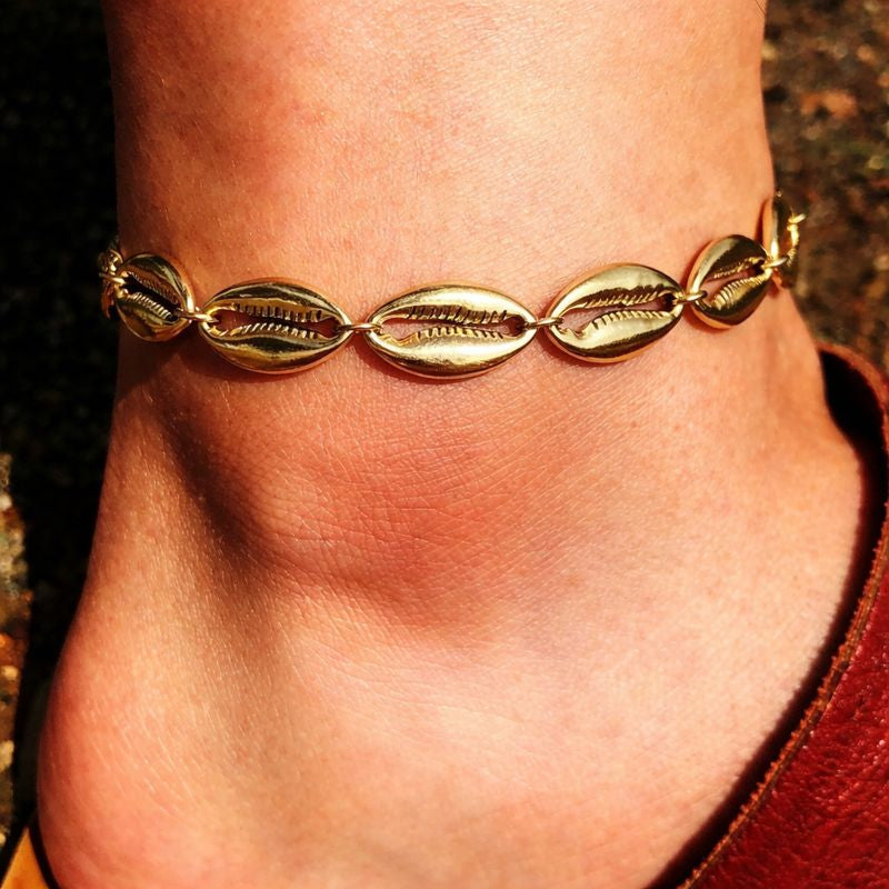A bold and trendy gold imitation anklet crafted with polished cowrie shell charms, perfect for making a statement during a tropical getaway or a casual summer day out.