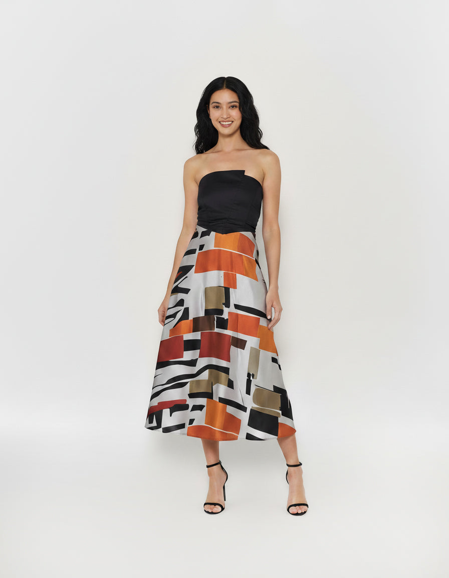A-line silhouette dress showcasing a silky satin skirt with a bold geometric block print in vibrant orange, deep red, and neutral earth tones.