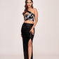 Model in a one-shoulder printed crop top and black ankle-length skirt with a daring slit, exuding poised elegance in a relaxed stance.