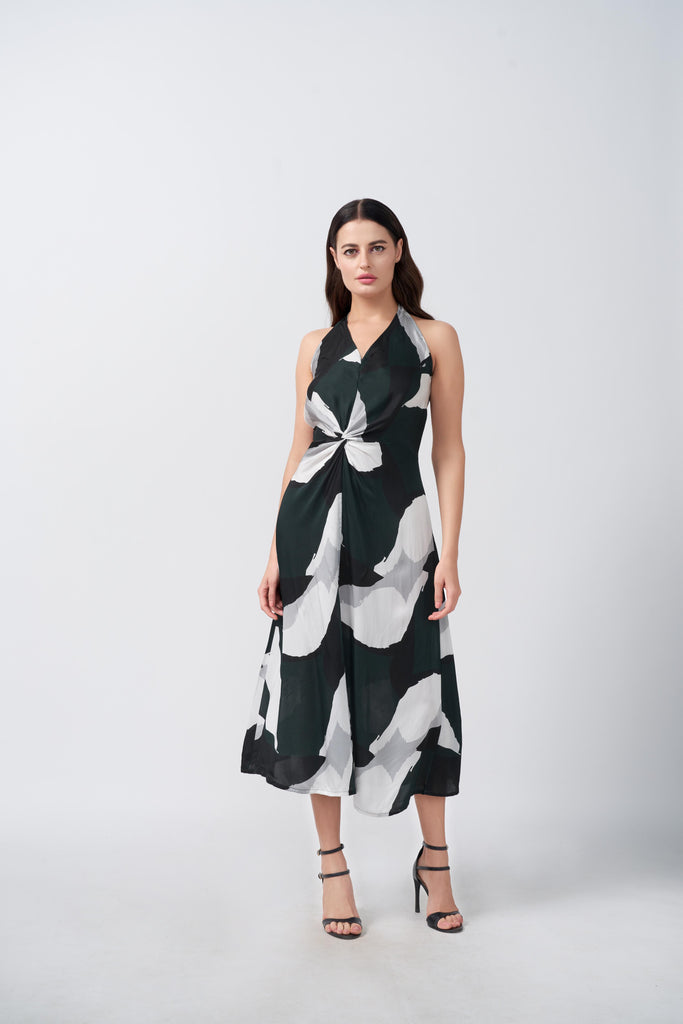 Model facing front in a deep green and white abstract print satin dress with halter neck and asymmetrical hemline.