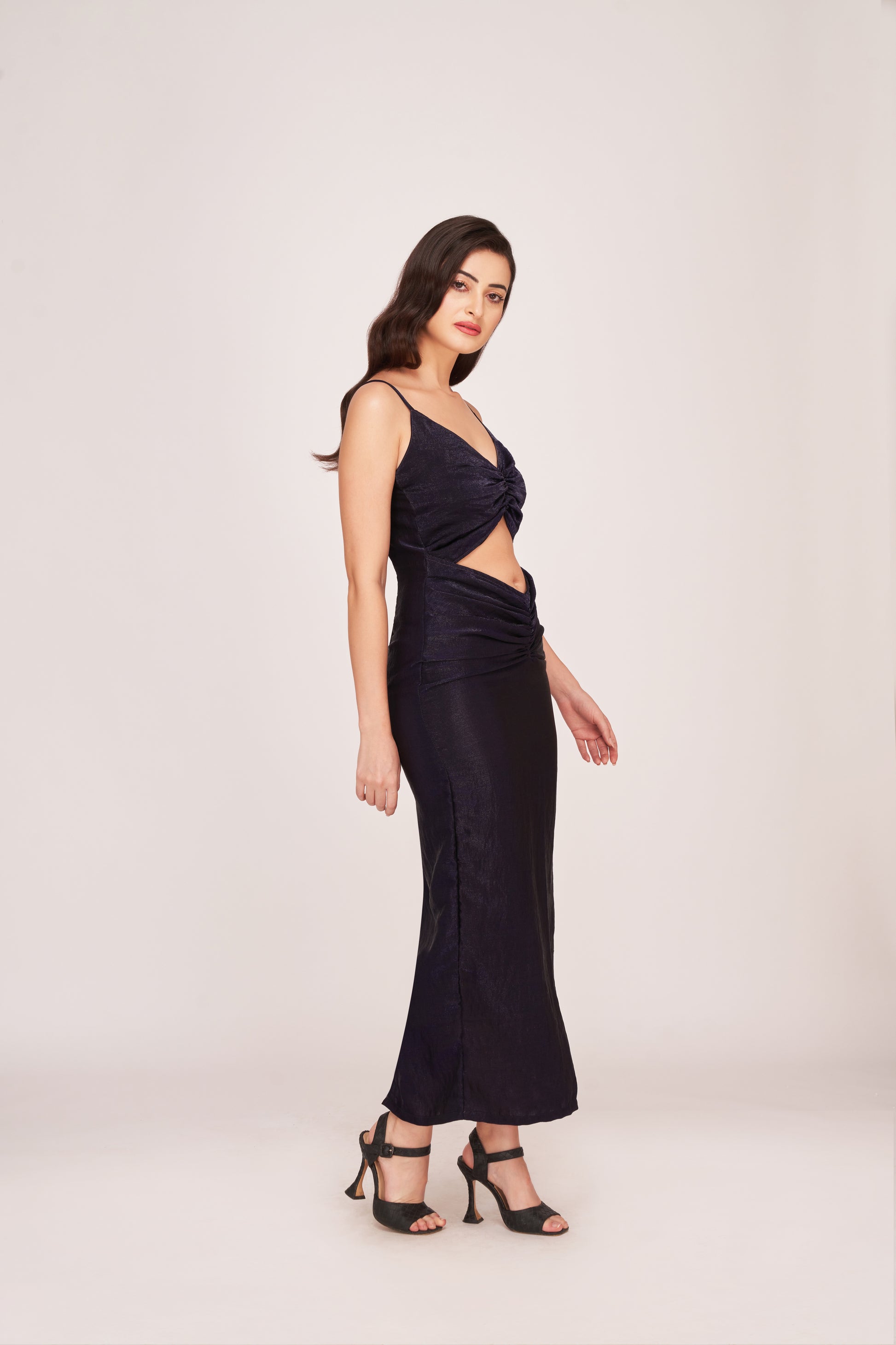 Angled view of model with one hand on hip in a fitted purple crepe dress with diamond cut-out and shoulder straps.